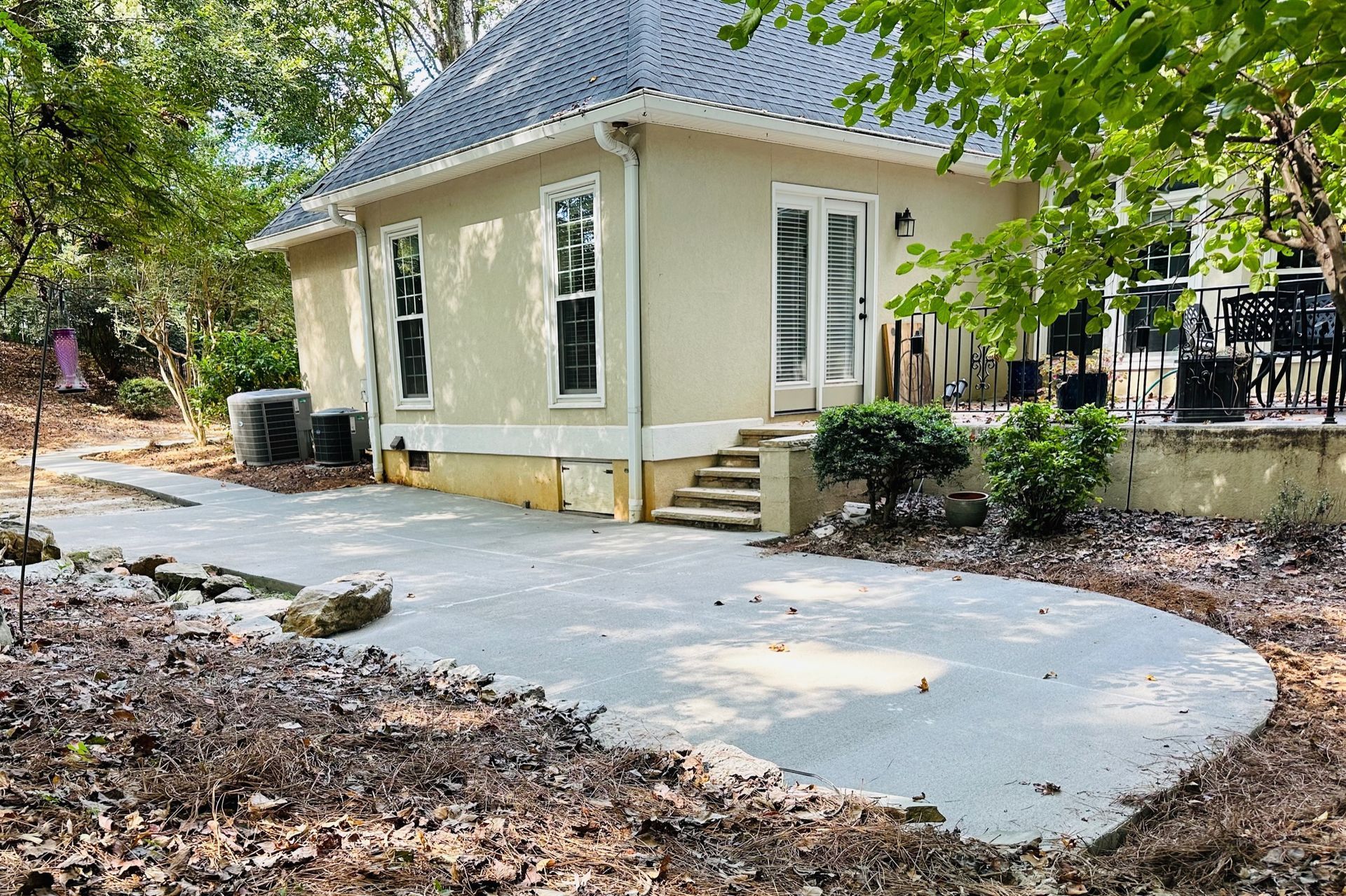 Small yellow house with white trim and a curved concrete walkway in a leafy yard