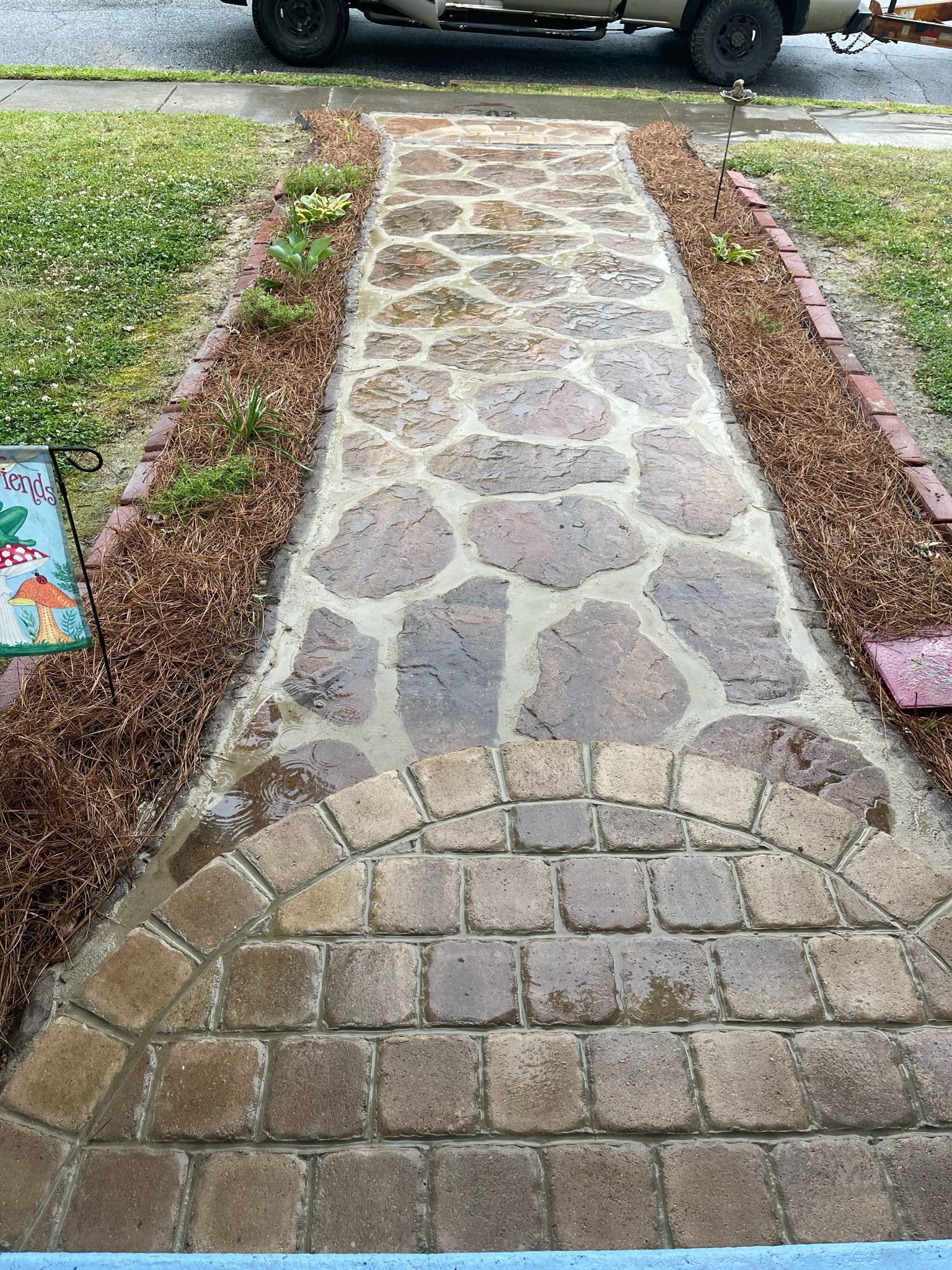 Stone and brick walkway leading to a street, bordered by brown mulch and grass.