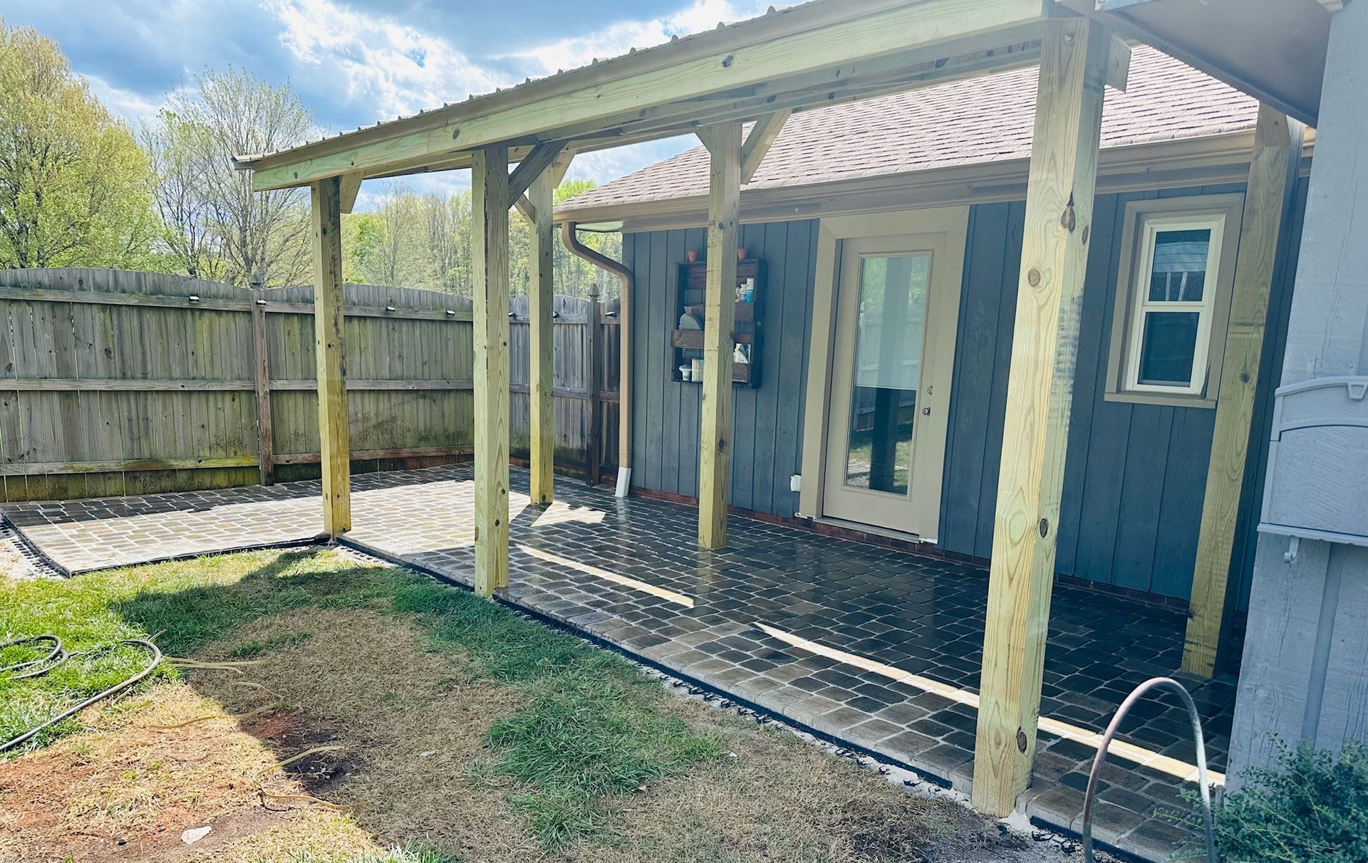 Wooden backyard porch with covered roof, blue siding, and gravel patio beside a fenced yard