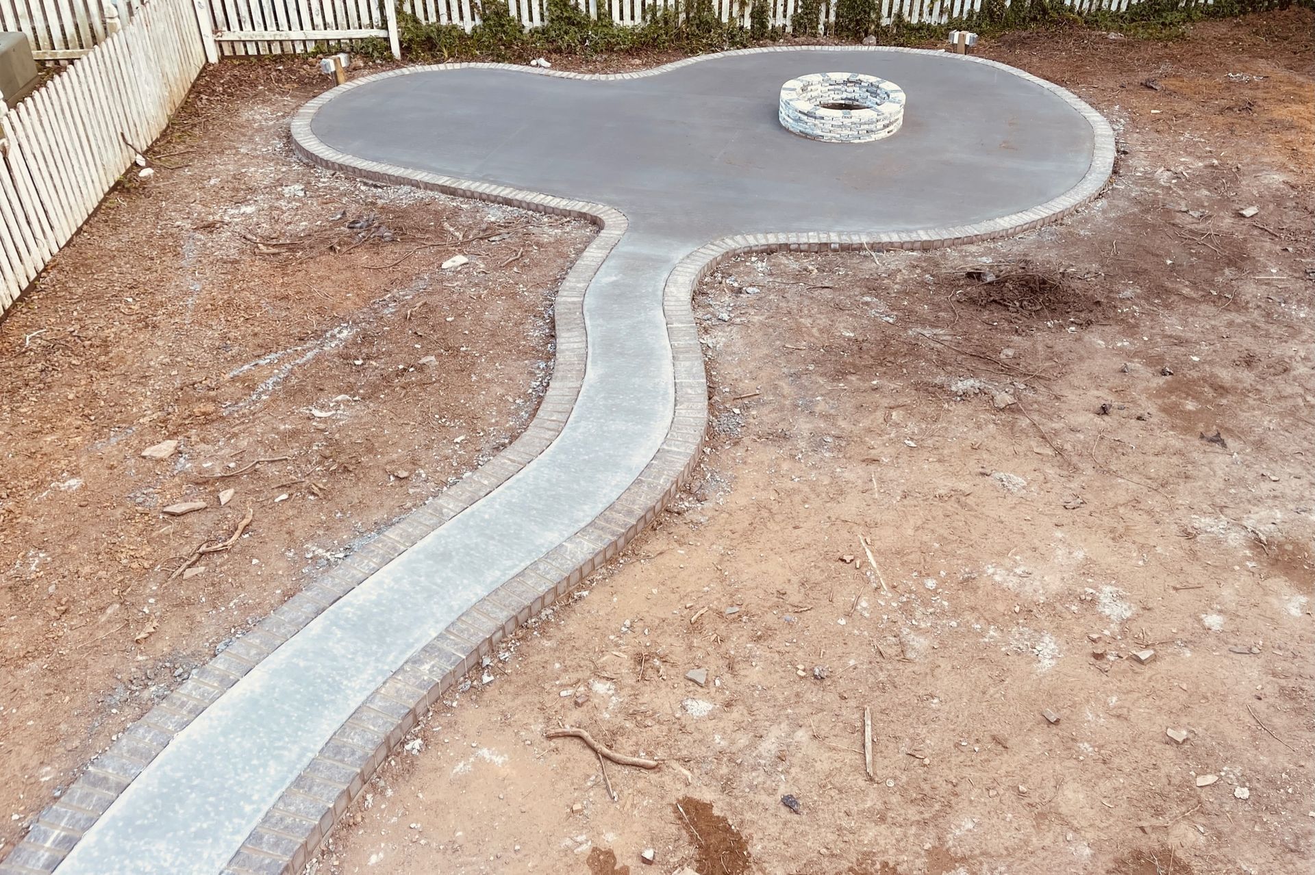 Concrete walkway through a bare yard leading to a circular patio with a small stone feature.