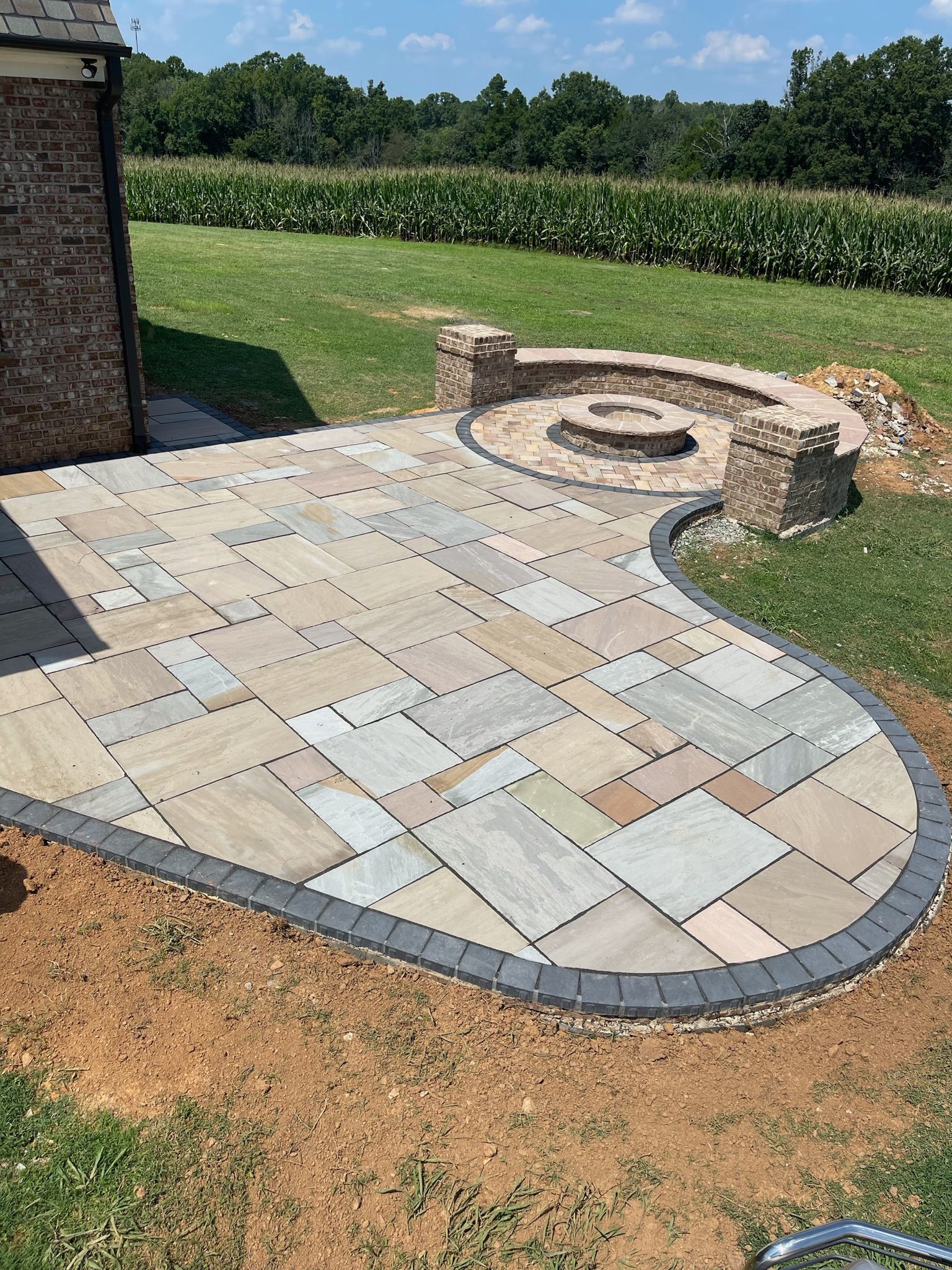 Patio with light stone pavers and circular stone seating beside a grassy yard and field