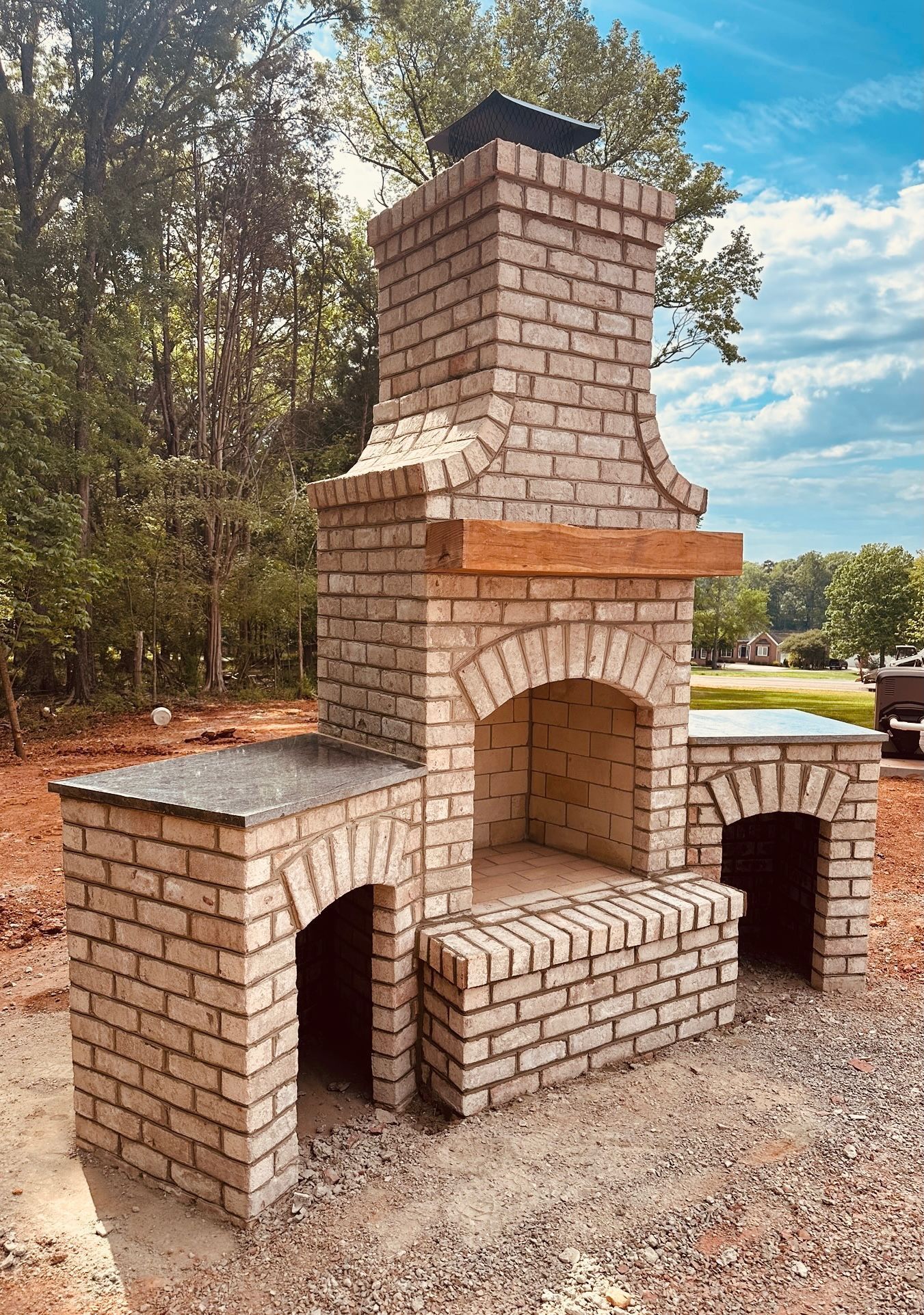Brick outdoor fireplace with chimney and arched openings on a gravel patio