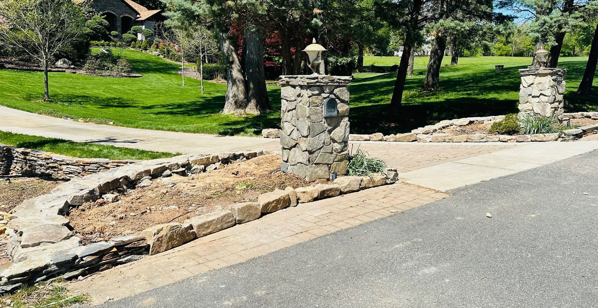 Stone entrance posts beside a paved road and grassy park path under bright sunlight