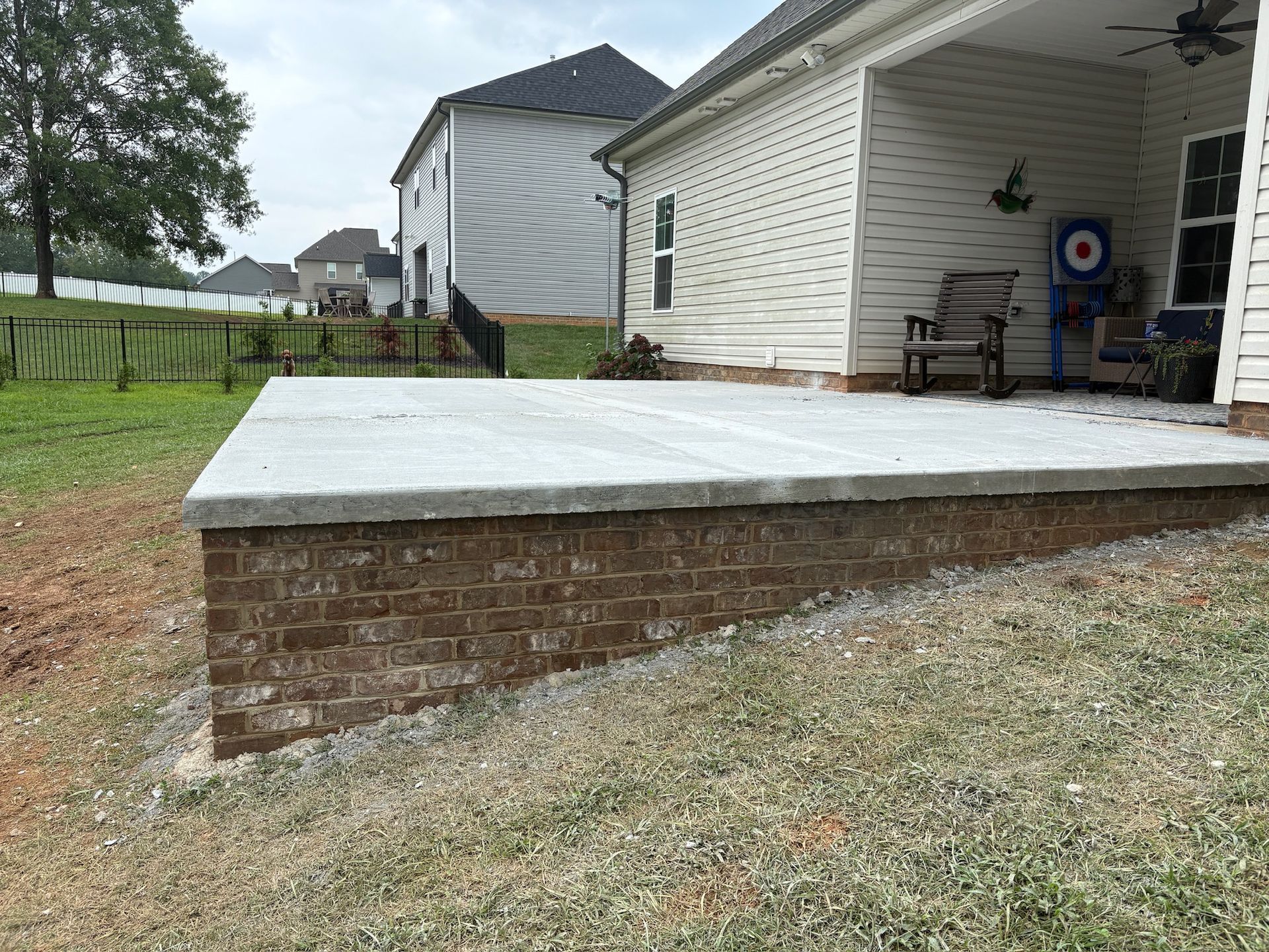 Brick-and-concrete backyard patio beside a white house with a covered porch