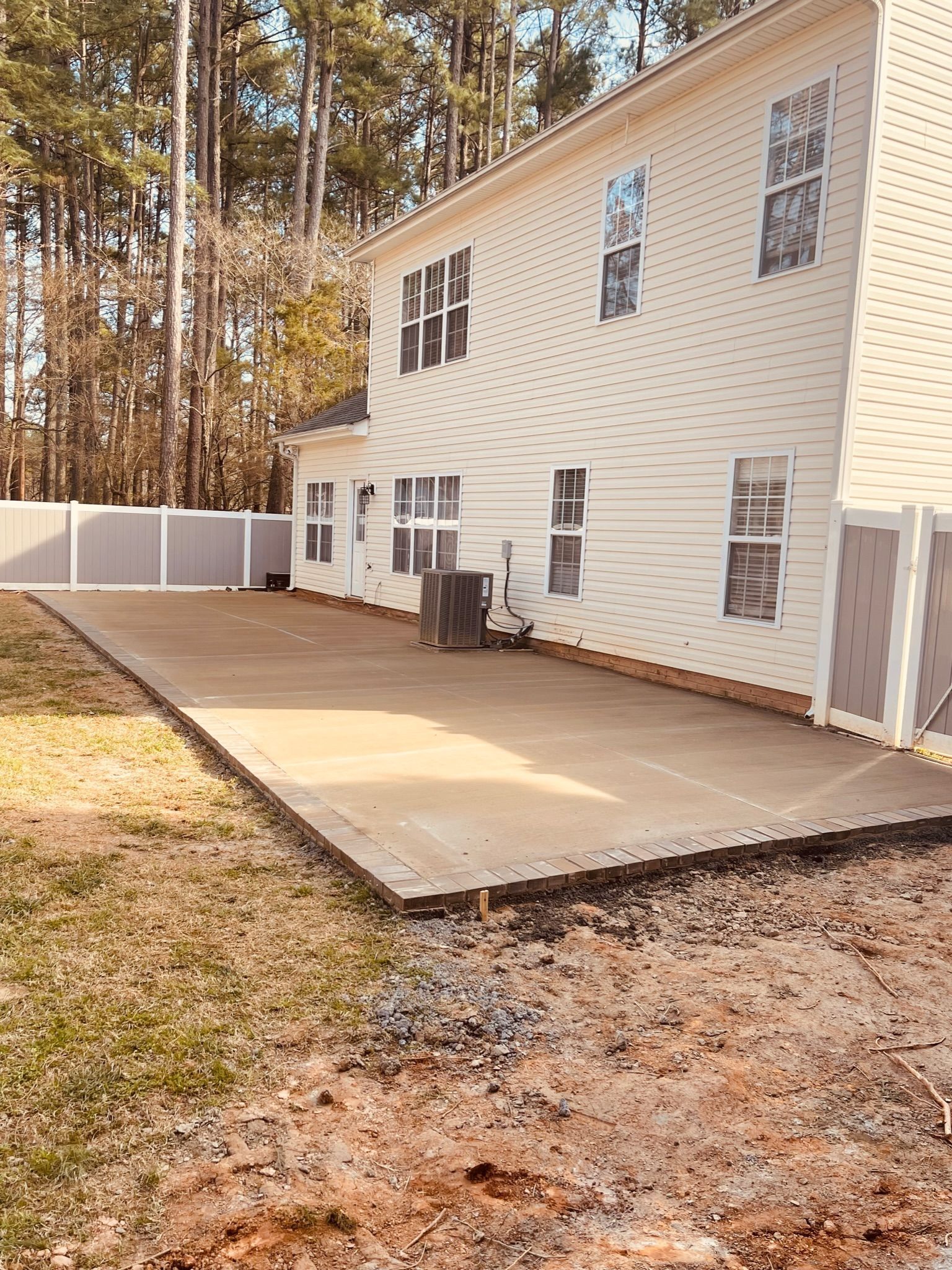 House exterior with white siding, a concrete patio, and a fenced backyard with trees.