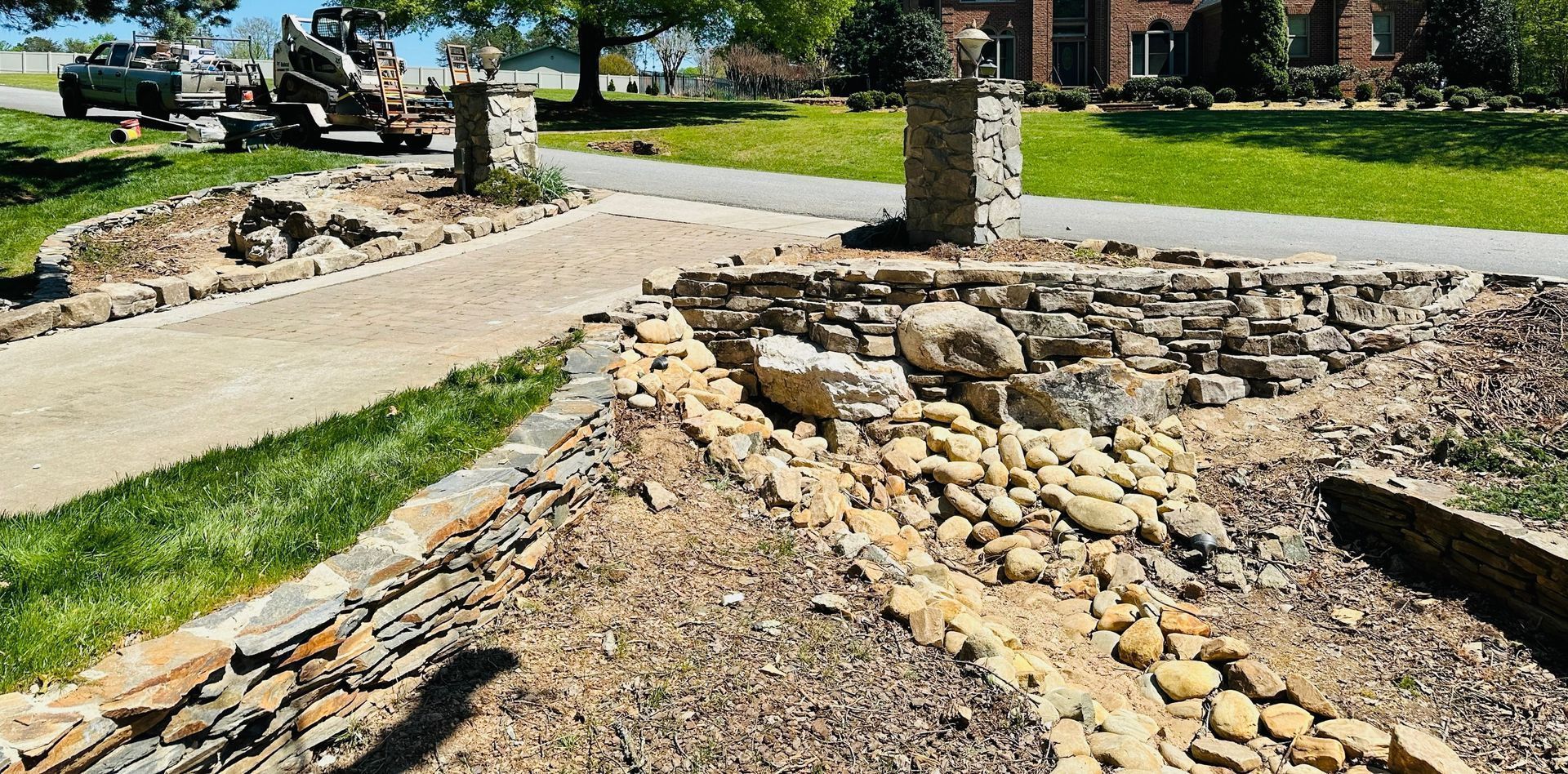 Stone-lined garden landscape with a dry creek bed beside a paved path and lawn.