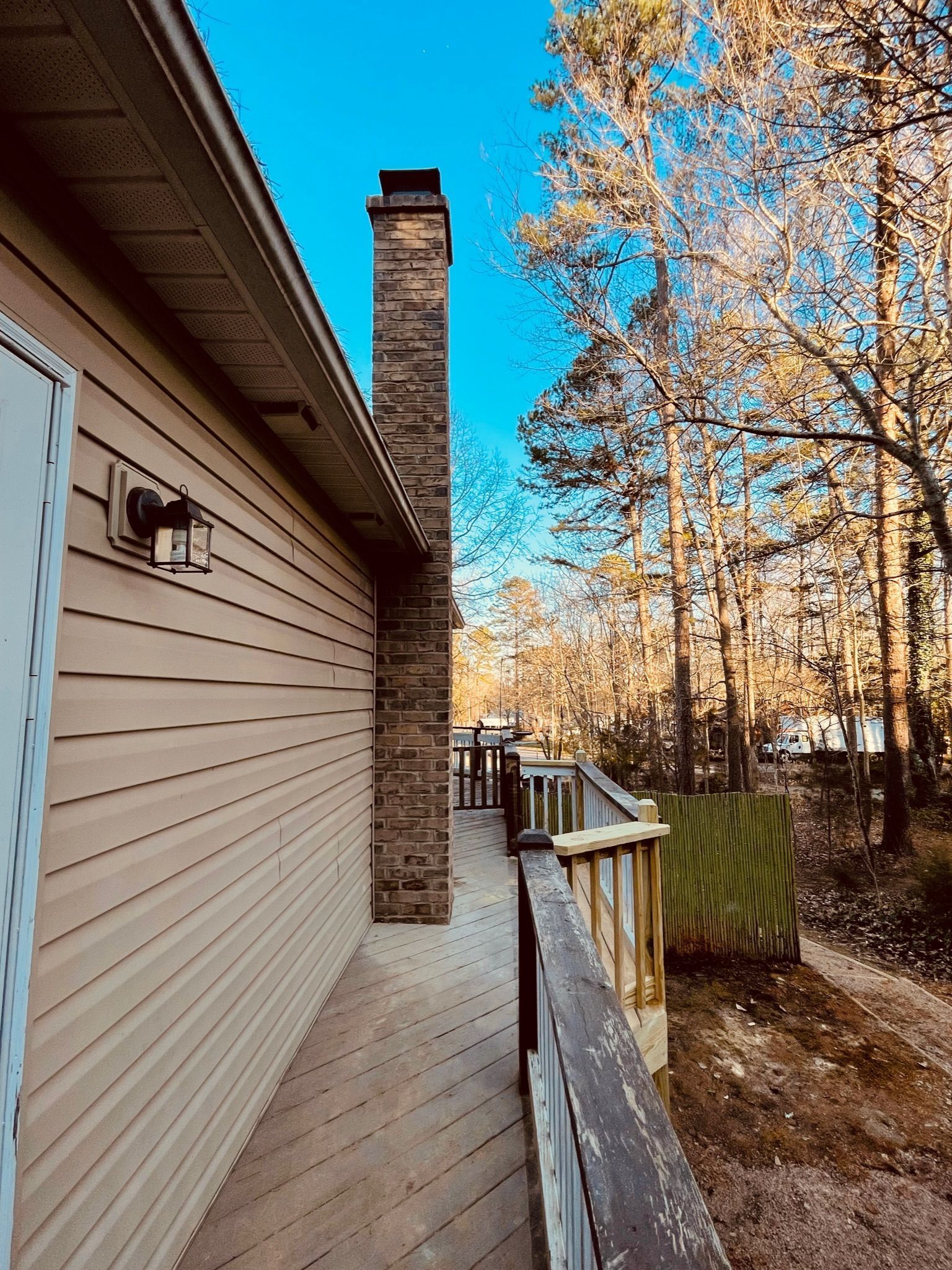 Side porch beside a brick chimney, with white siding and autumn trees under a blue sky.