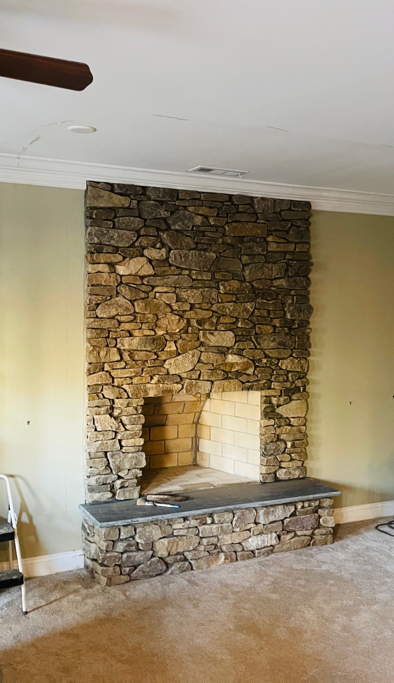 Stone fireplace with built-in hearth and mantel in a beige room with carpeted floor
