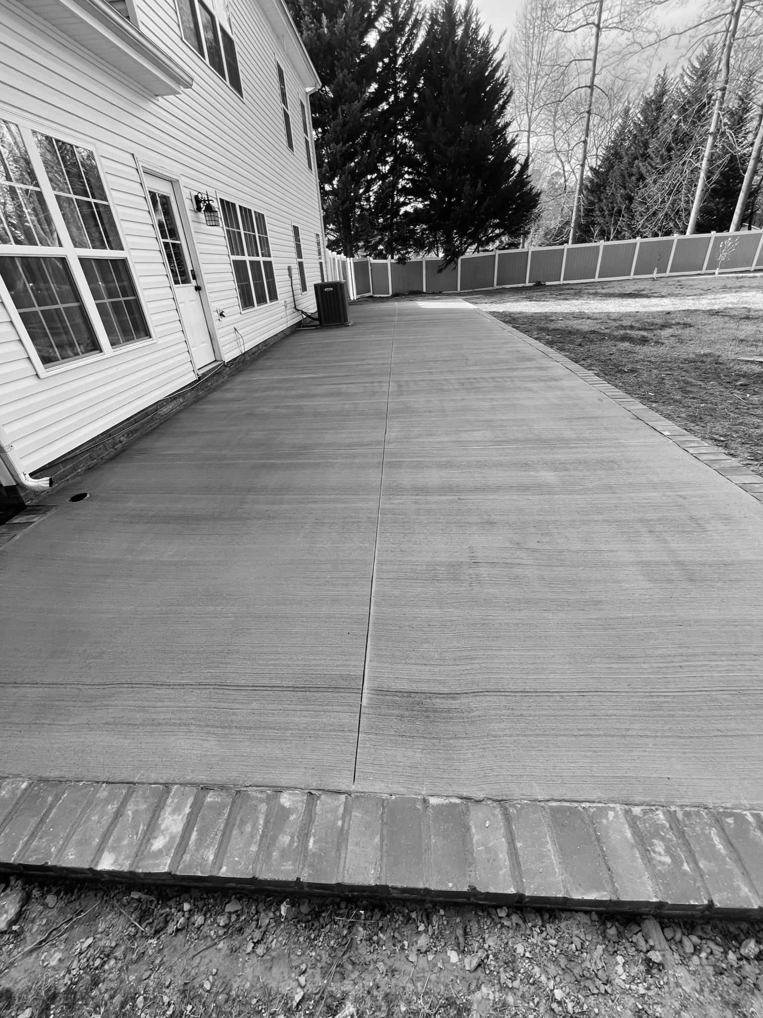 Wooden walkway beside a white house, leading toward trees and a fenced yard.