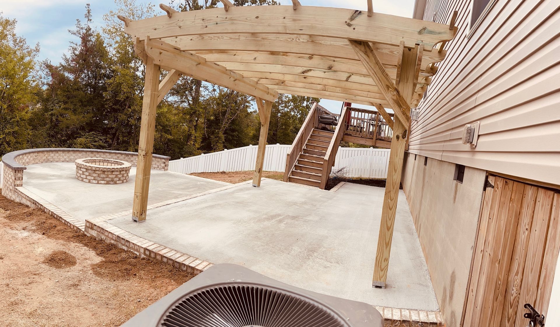 Backyard patio with white pergola, concrete slab, stairs, and house siding.
