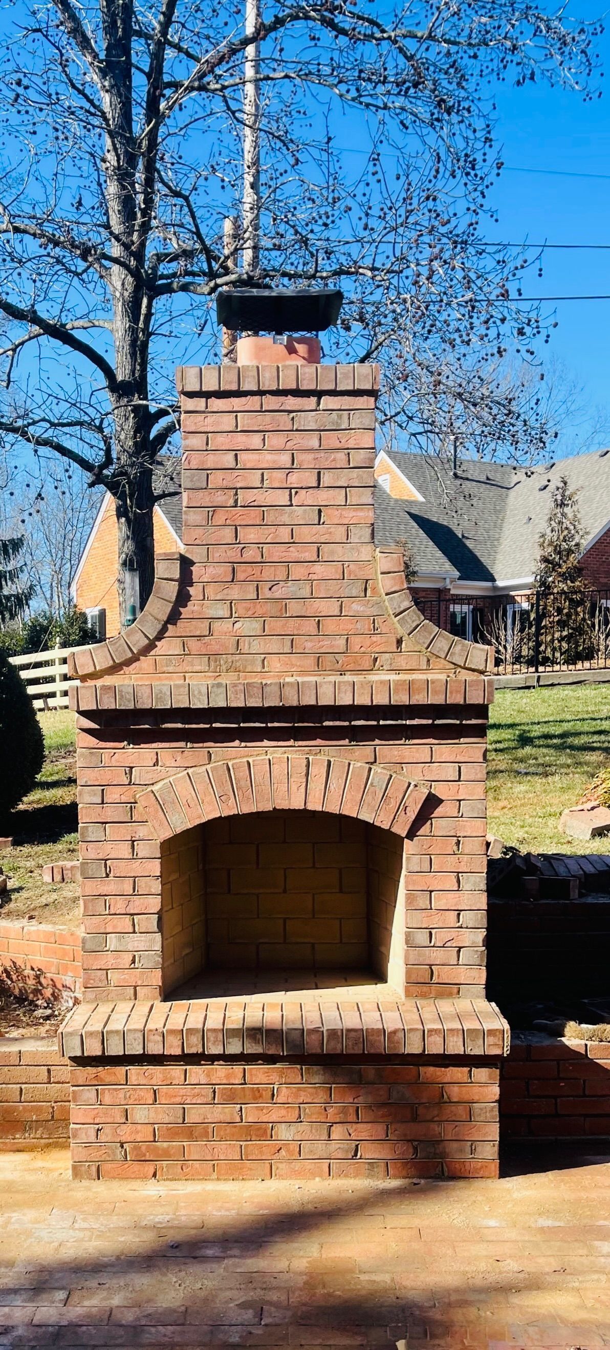 Brick outdoor fireplace with arched opening and chimney in a sunny yard