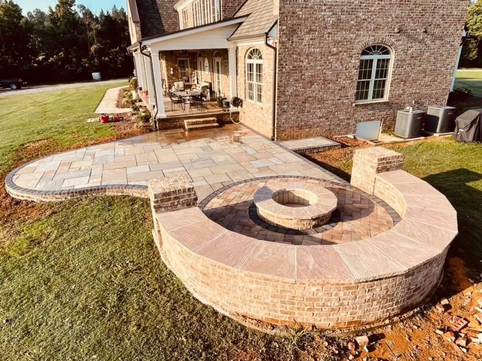 Backyard stone patio with circular fire pit beside a brick house and covered porch