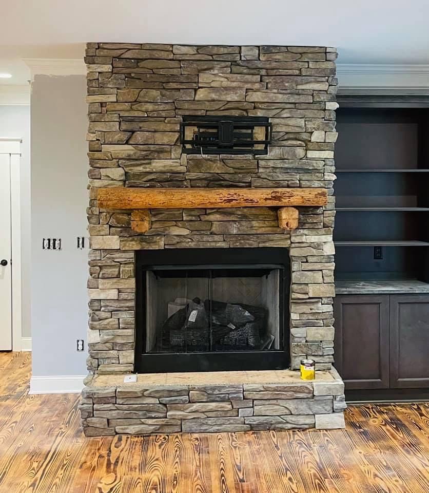 Stone fireplace with wood mantel and black firebox in a living room, beside built-in shelving.