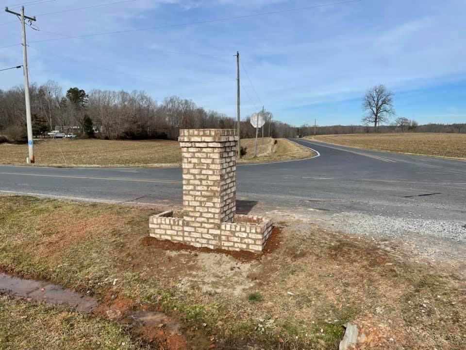 Brick roadside mailbox pillar beside a rural intersection under a clear blue sky
