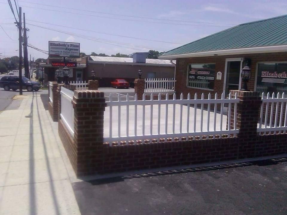 Brick-and-white fence along a sidewalk beside a green-roofed building on a sunny street