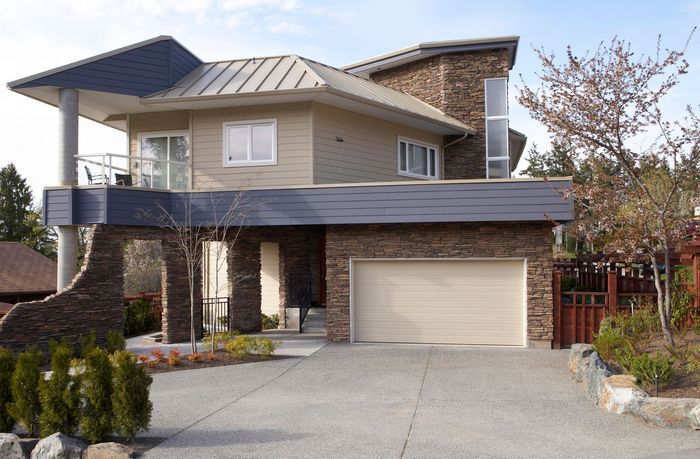 Modern two-story house with stone facade, tan siding, and a two-car garage. 
