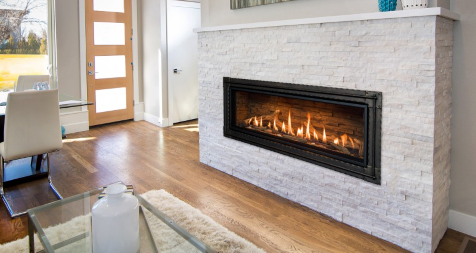 Fireplace with lit flames in a white stone wall, in a living room with wooden floors.