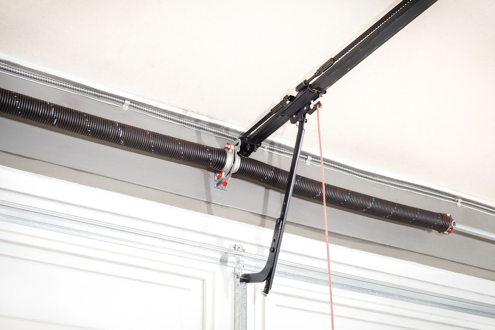 Garage door opener mechanism with a black rail, spring, and red cord.
