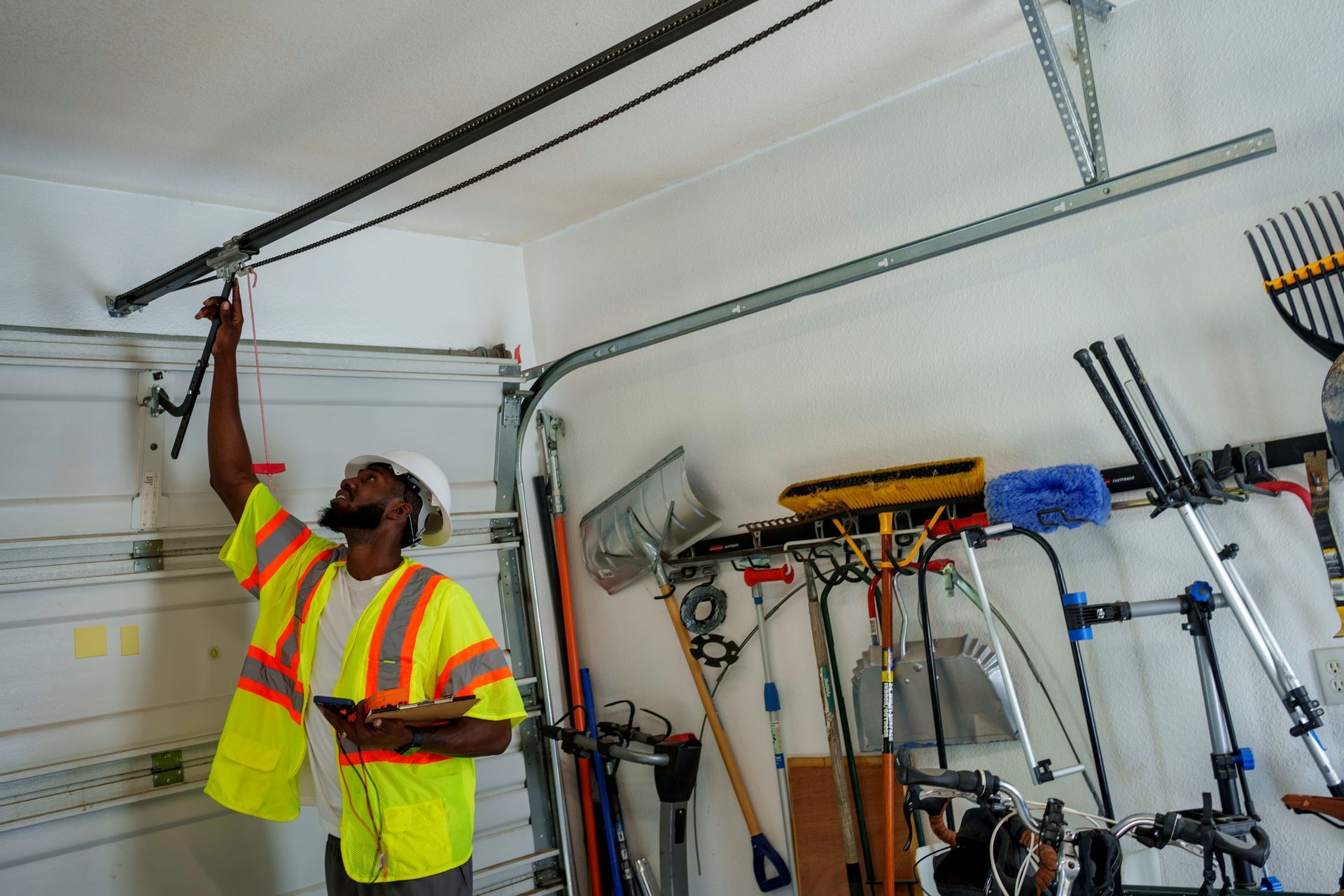 Person in safety vest inspecting a garage door opener in a garage.