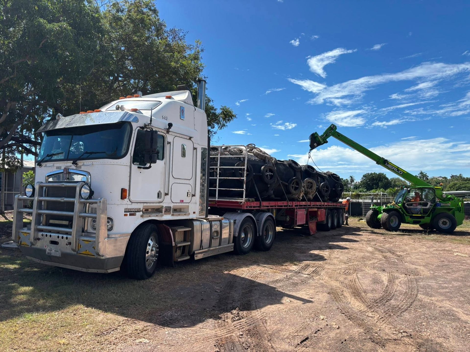 A Large White Truck Is Parked and A Green Crane Is Lifting Materials on The Trailer