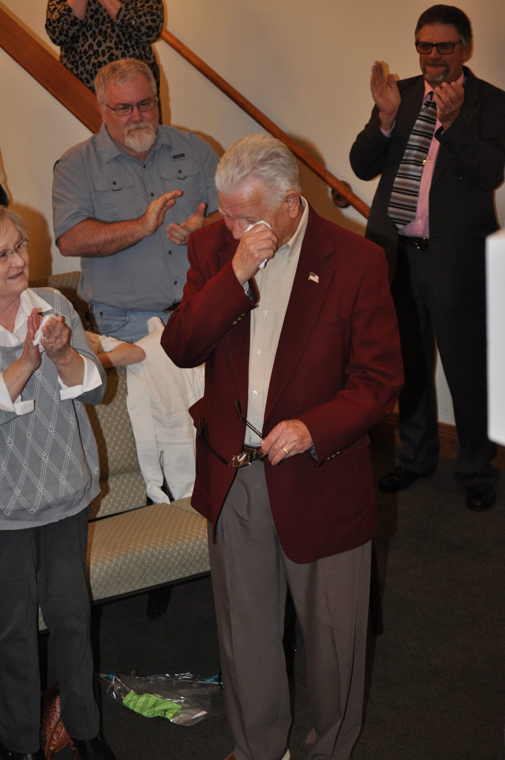 Man in maroon blazer wipes tears, surrounded by people applauding indoors.