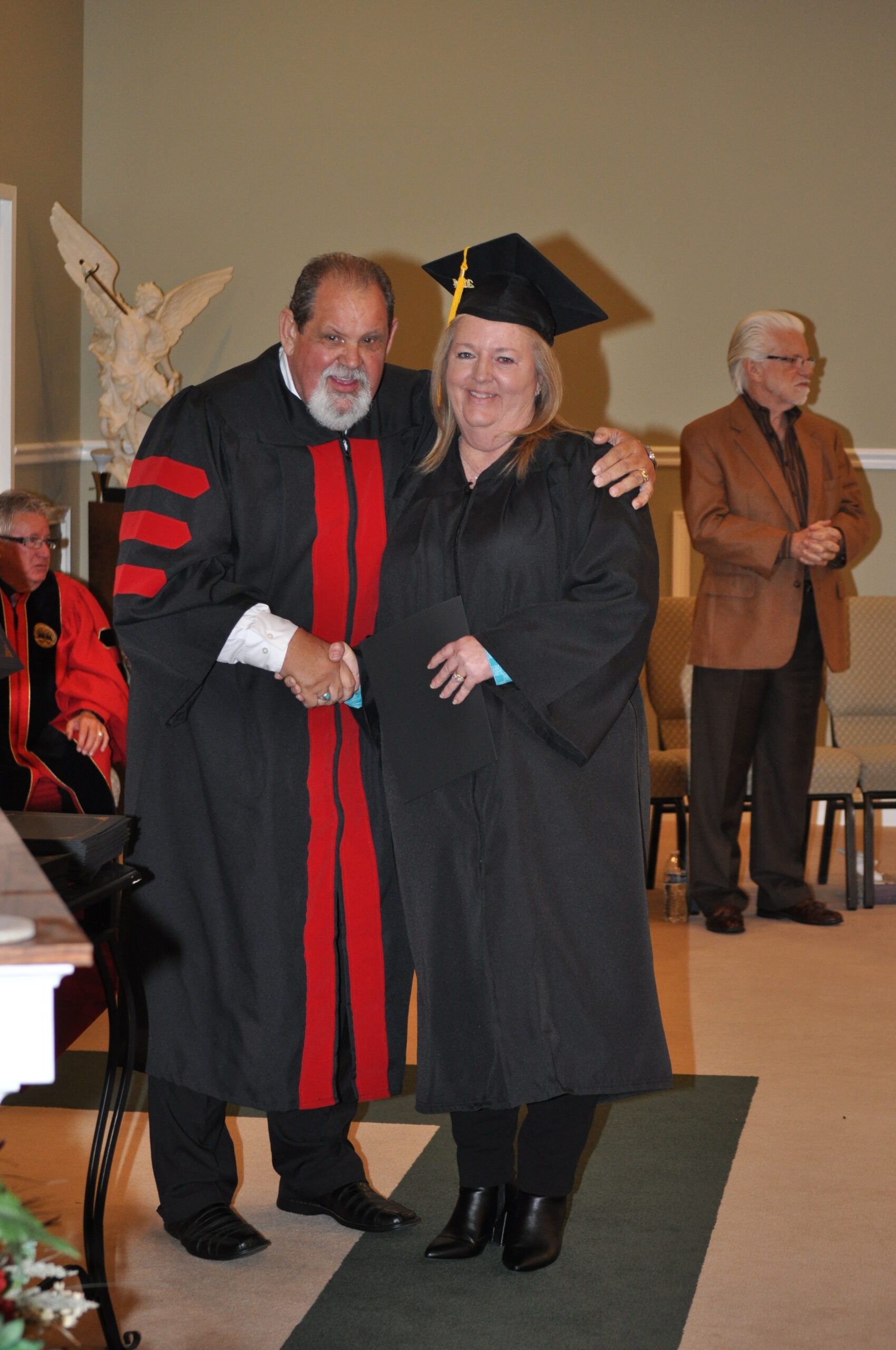 A graduate in a cap and gown shaking hands with a robed man at a ceremony.