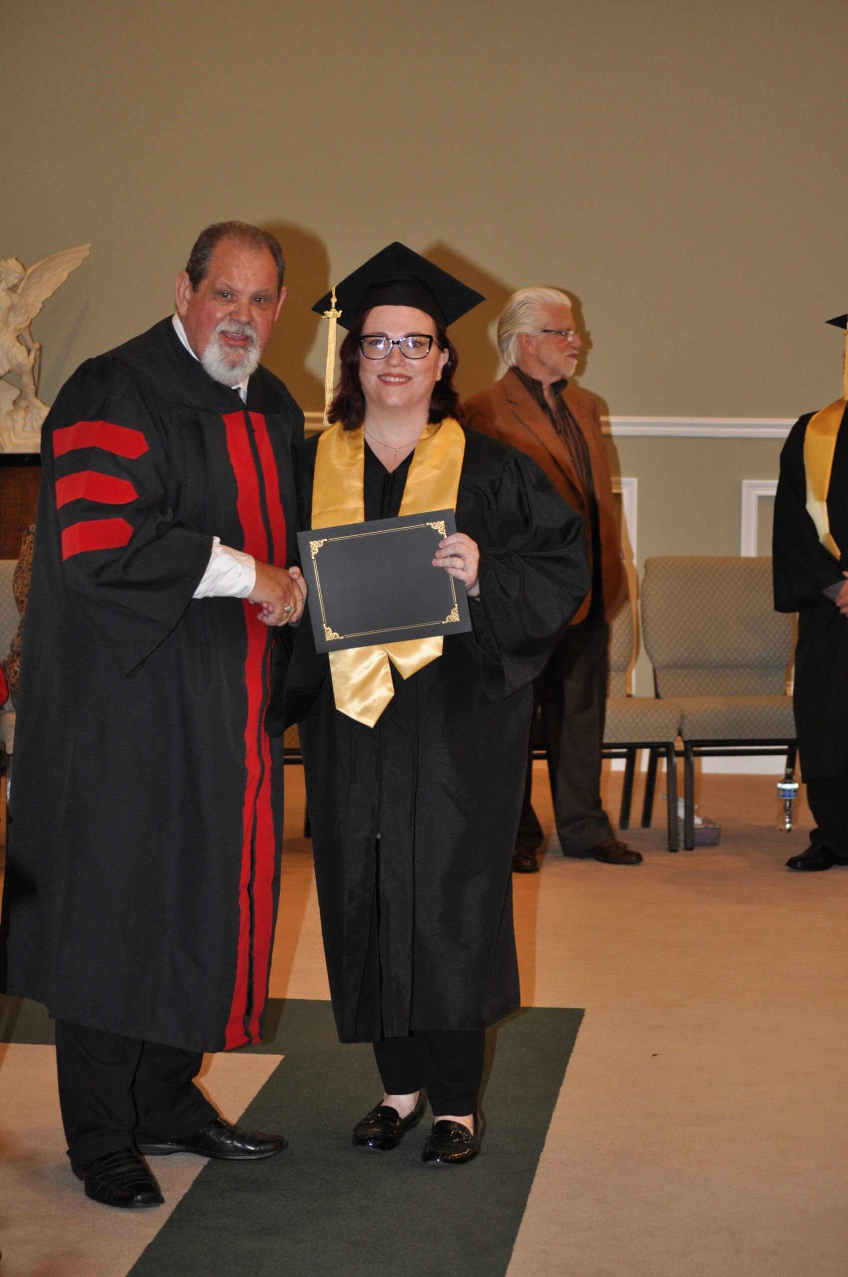 Graduation: A woman in cap and gown receives a diploma from a robed person.