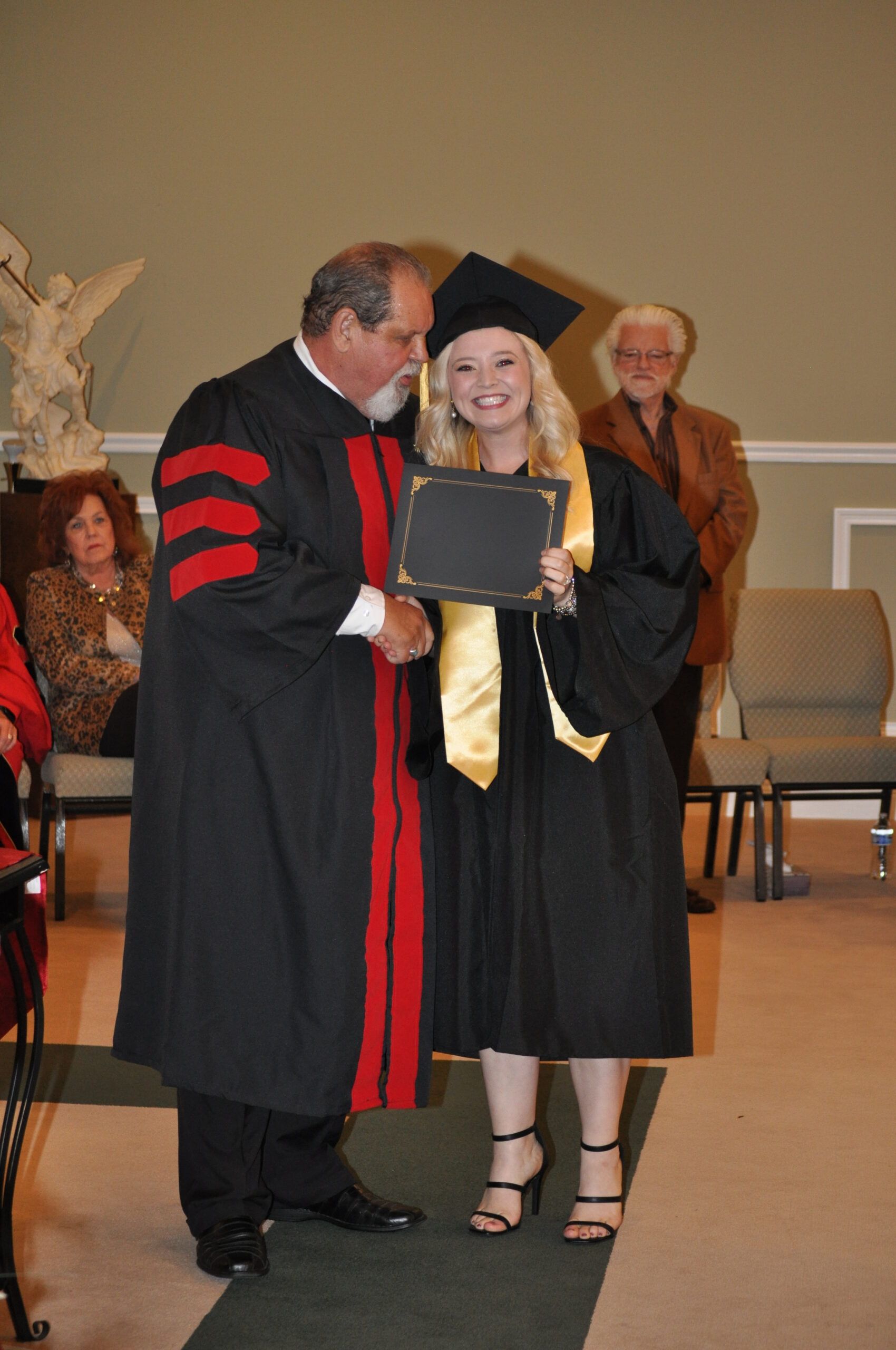 A graduate receives her diploma from a robed man at a ceremony.