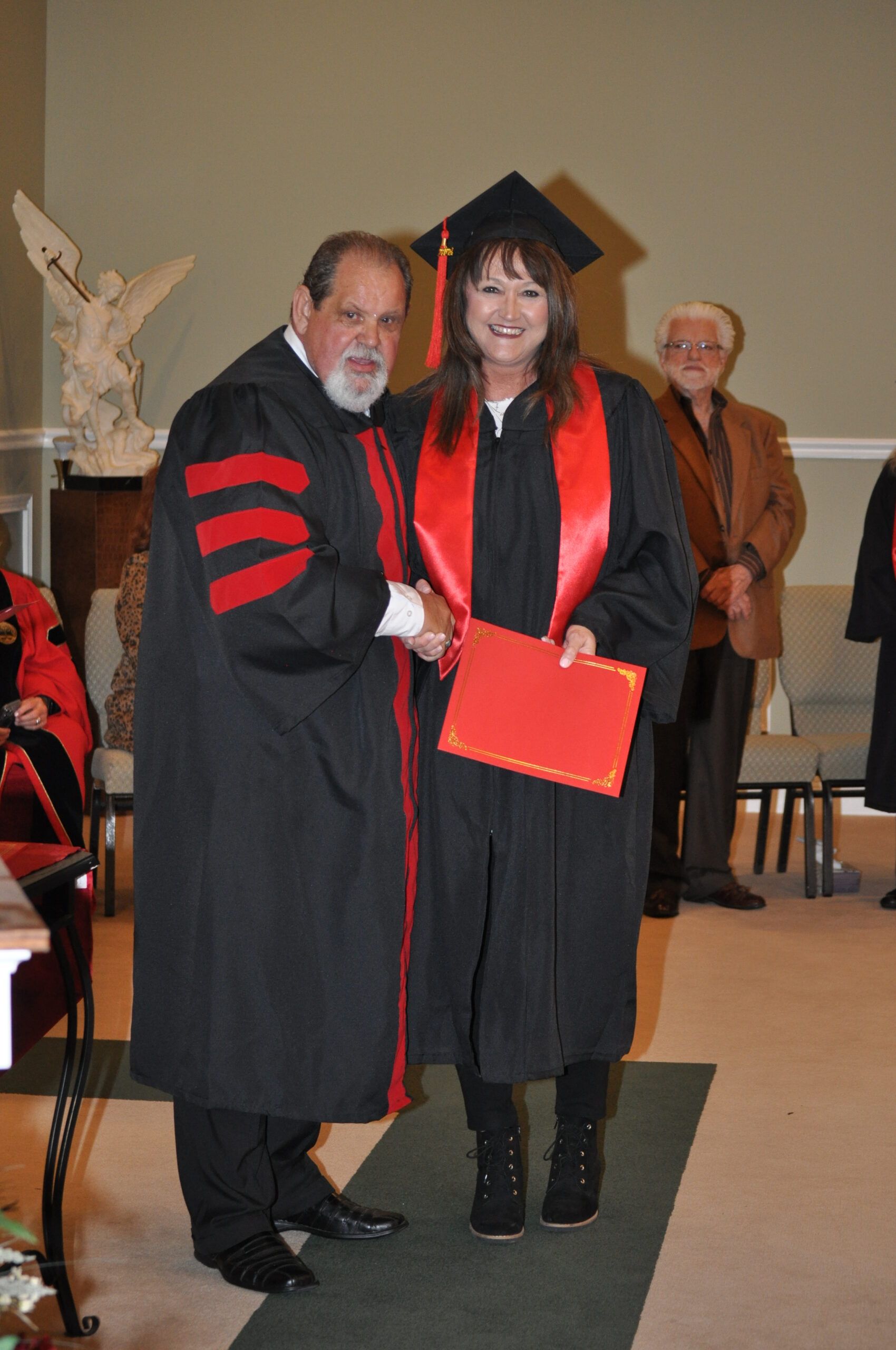 Person in graduation gown shaking hands with another person; inside setting.