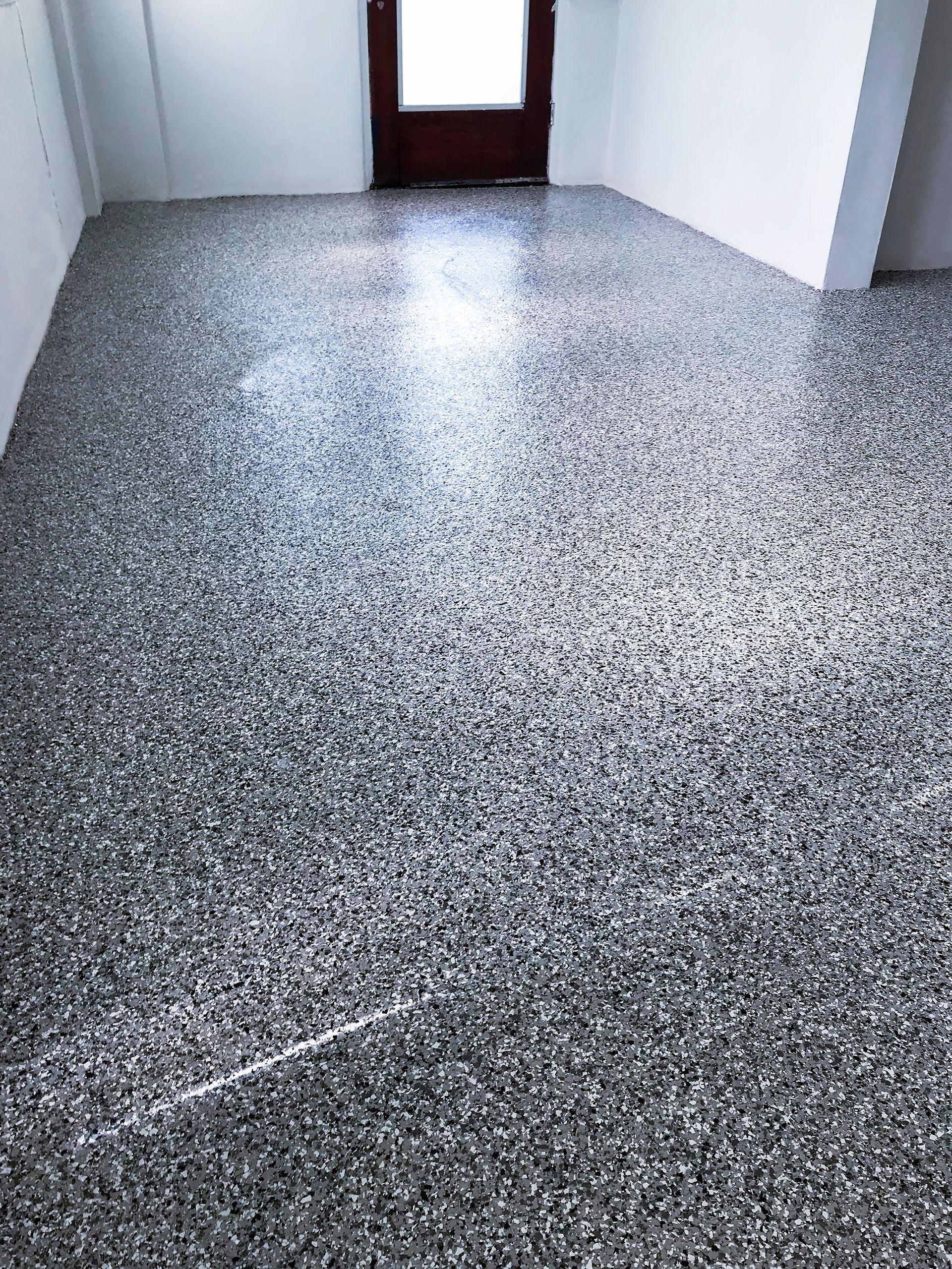A newly finished epoxy-flake floor in a room with white walls and a dark wooden door.