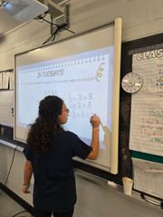 Teacher writing on a classroom whiteboard during a lesson.