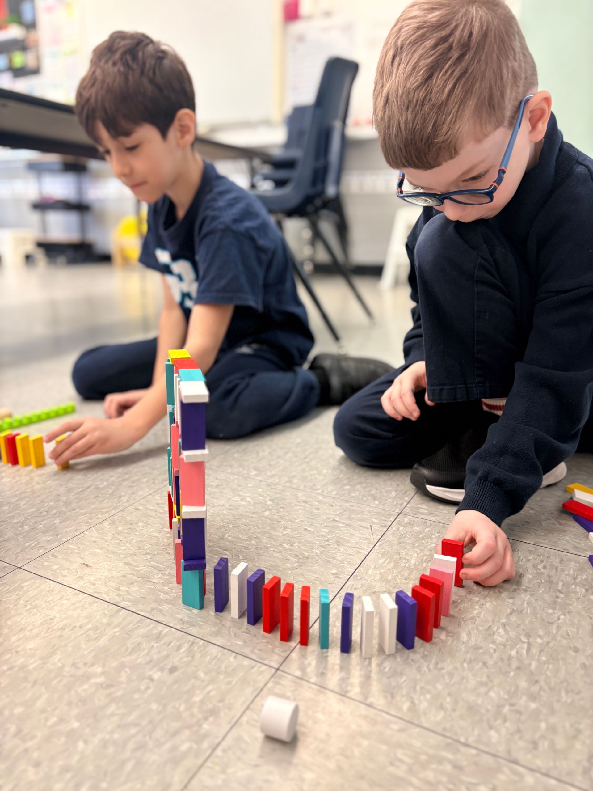 Child in a classroom points at blue counting pieces on a table next to a wooden tray of shapes