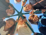 Smiling friends huddle in a circle, holding onto a playground structure against a blue sky.