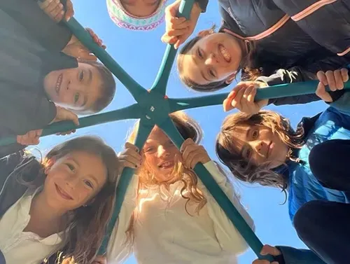 Smiling friends huddle in a circle, holding onto a playground structure against a blue sky.