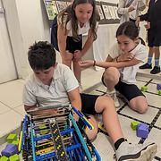 Children gathered around a robotics kit on the floor, assembling parts in a classroom.