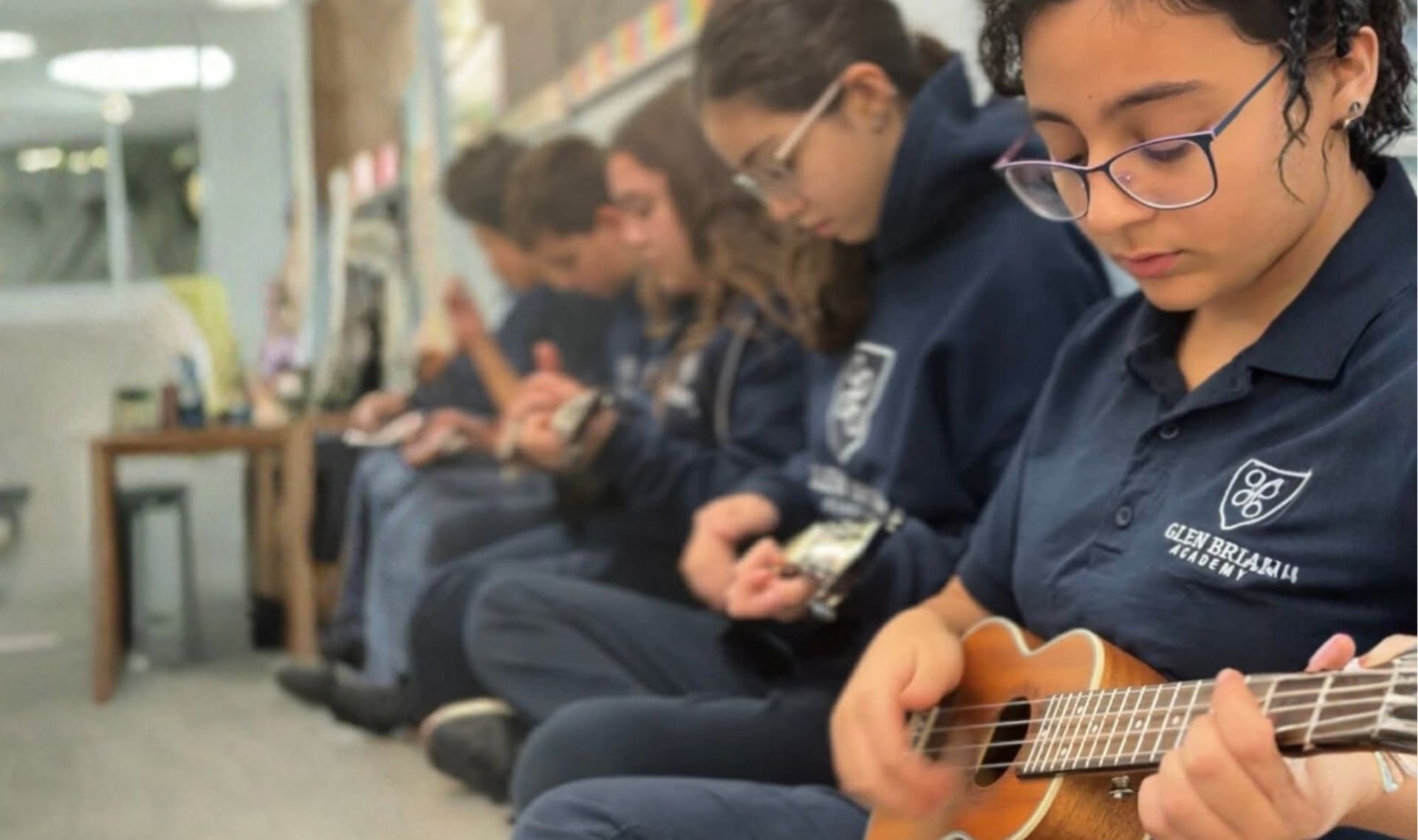 Students seated against a wall, concentrating while playing small string instruments.
