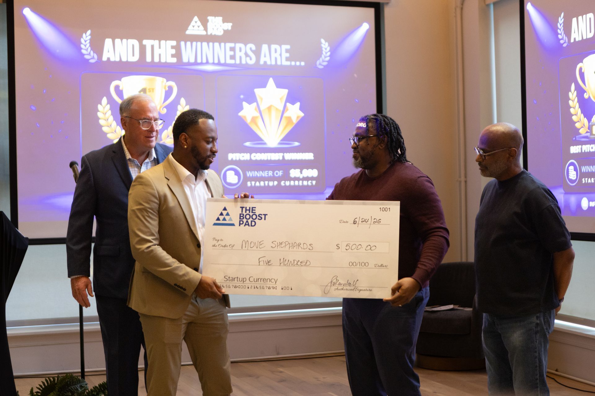 Four people on stage hold a large ceremonial check during an awards presentation.