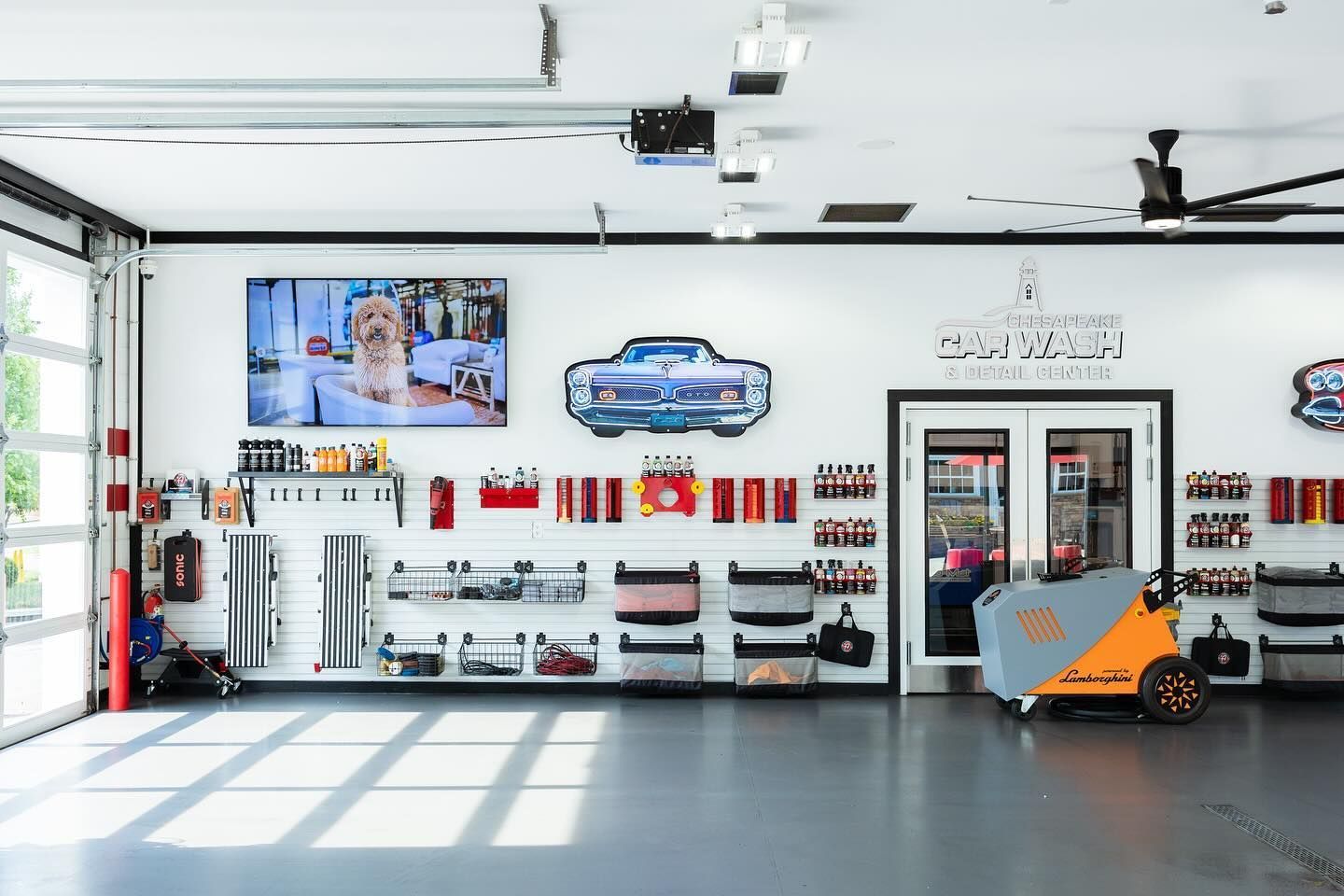 Interior of a car detailing shop; tools and products displayed on walls, a large screen, and a bright orange cart.