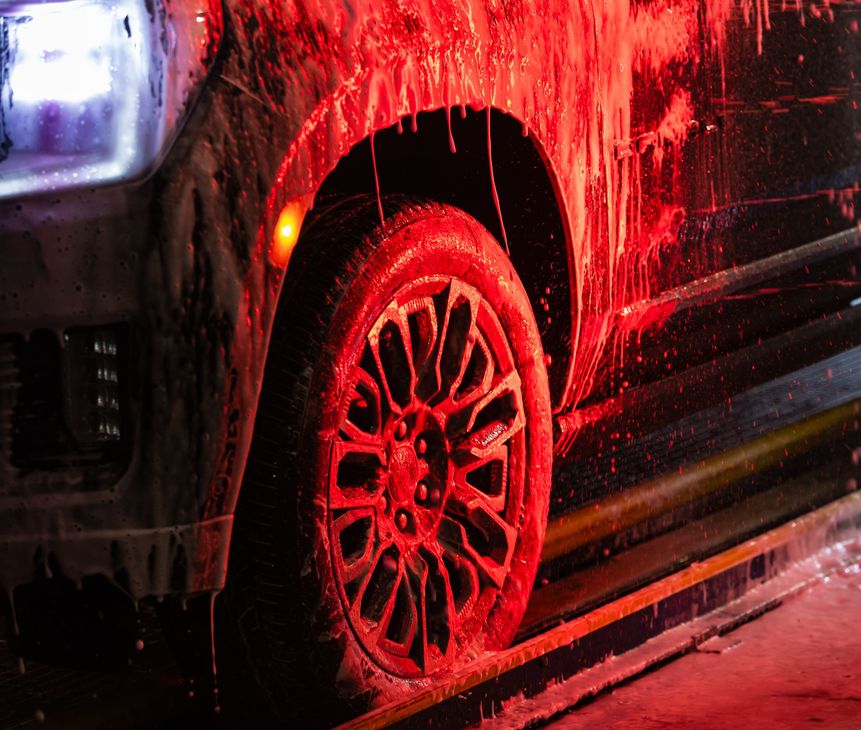Black vehicle being washed with red soapy water in a carwash, detail of front wheel.