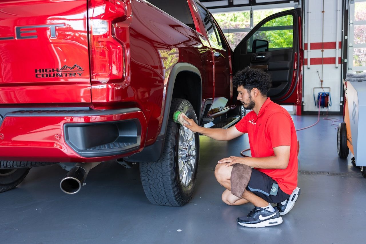 Mechanic inspecting the rear tire of a red pickup truck in an auto shop