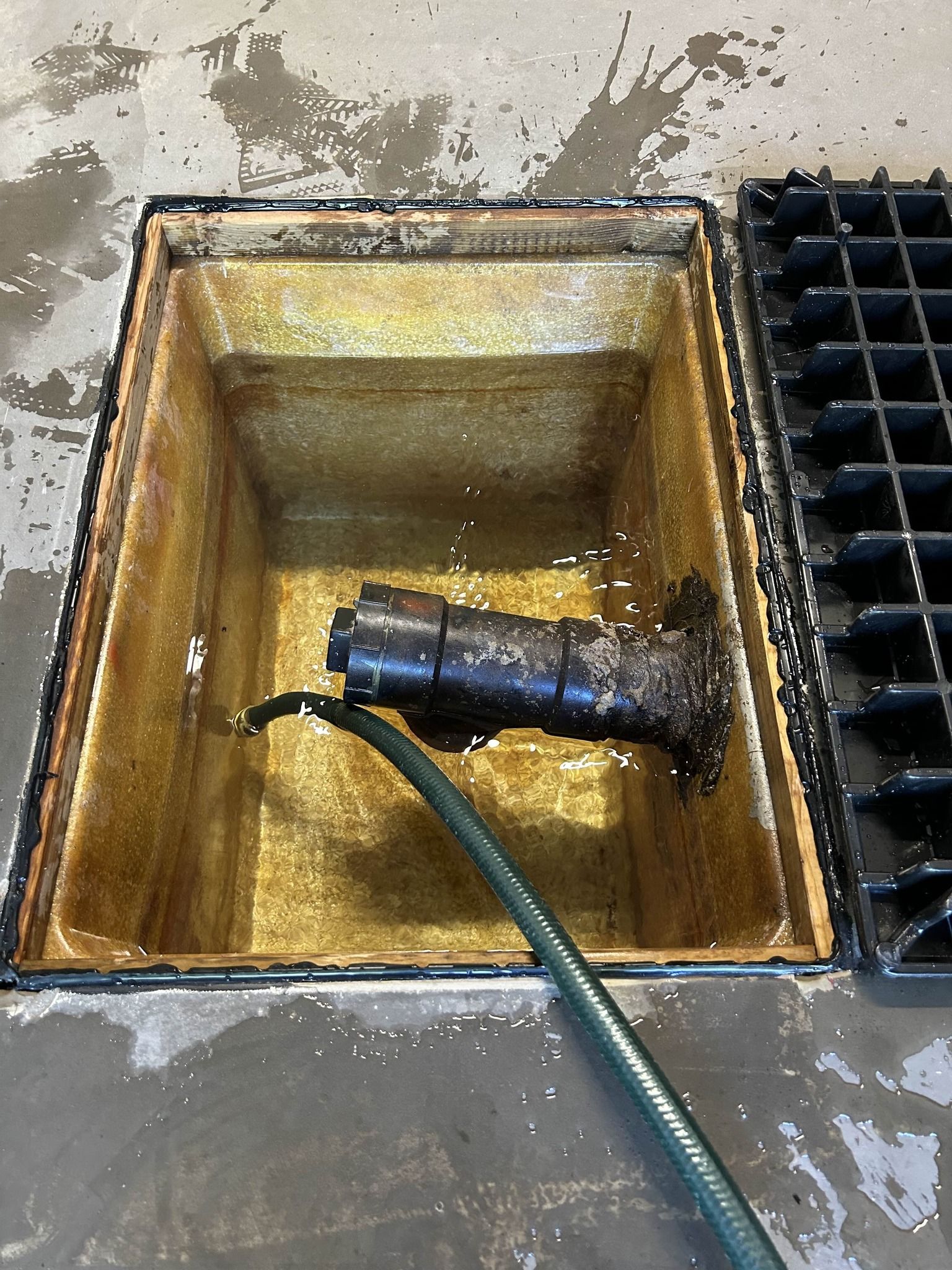Bassin utilitaire jaune rempli d'eau sale, tuyau noir et grille d'évacuation au sol à proximité