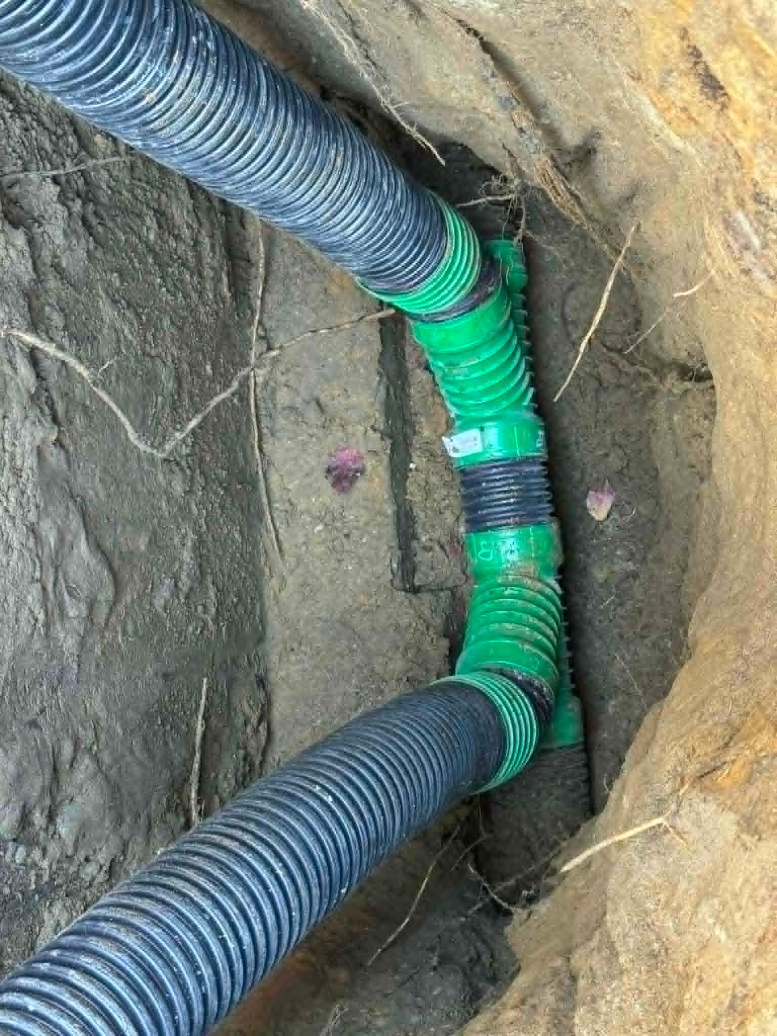 Des tuyaux ondulés verts et noirs étaient raccordés dans une tranchée souterraine.