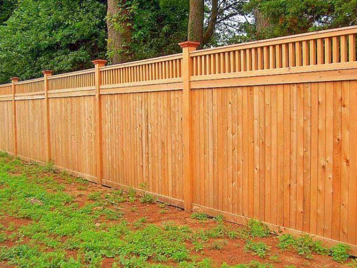 Wooden privacy fence with vertical planks, brown stain, and decorative top.