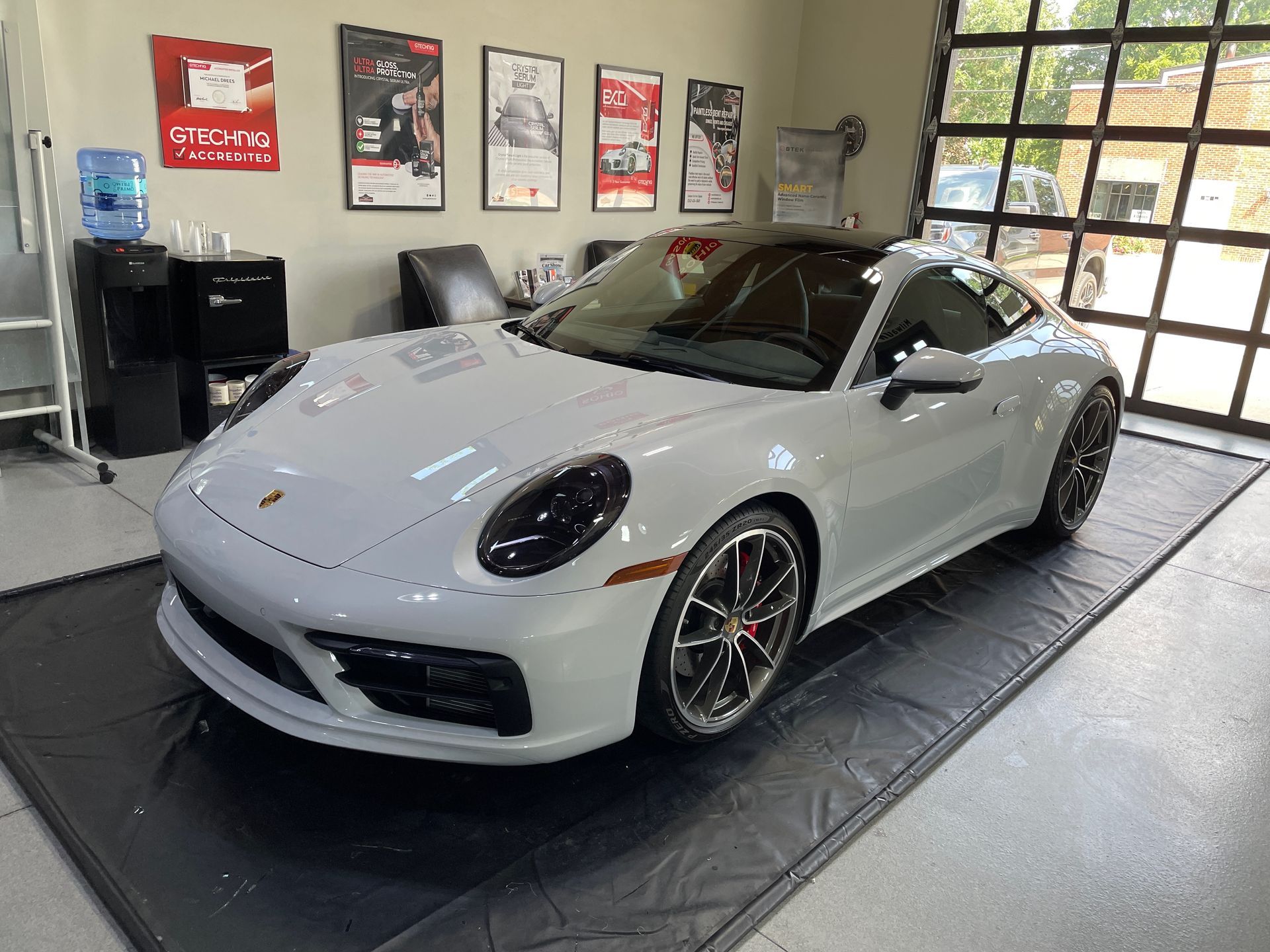 Light gray Porsche 911 coupe in a shop, parked on a protective mat. Dark tinted windows and black accents.