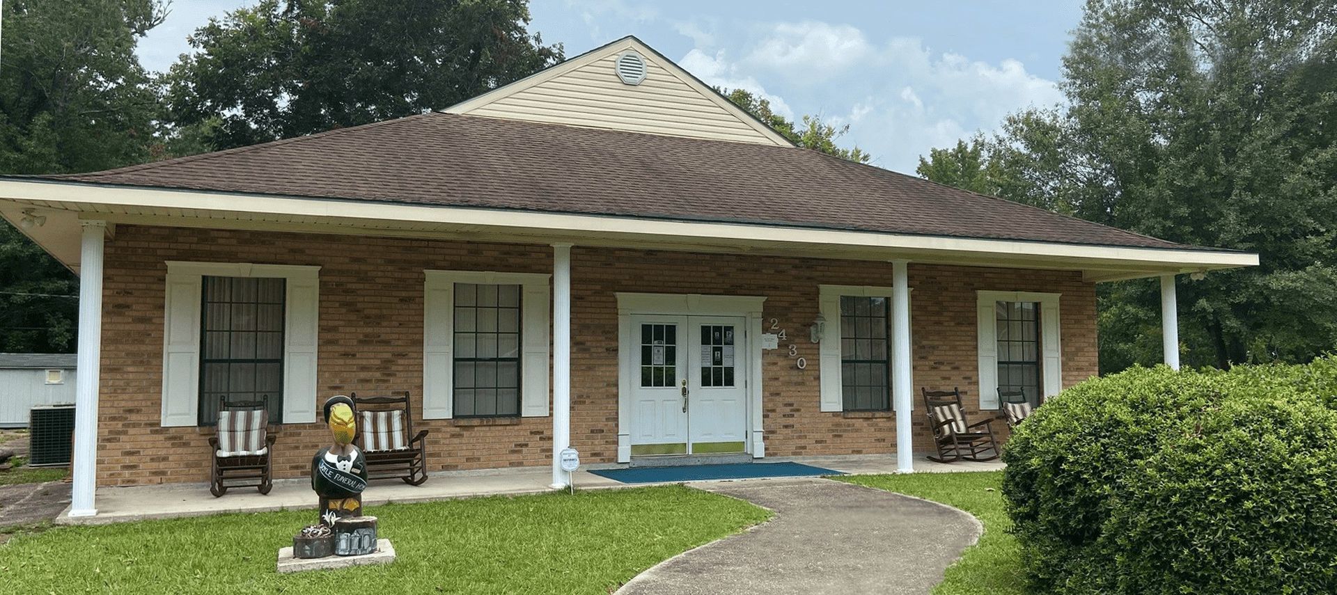 A low, light-colored building with a carport, American flag, and flowers in front.