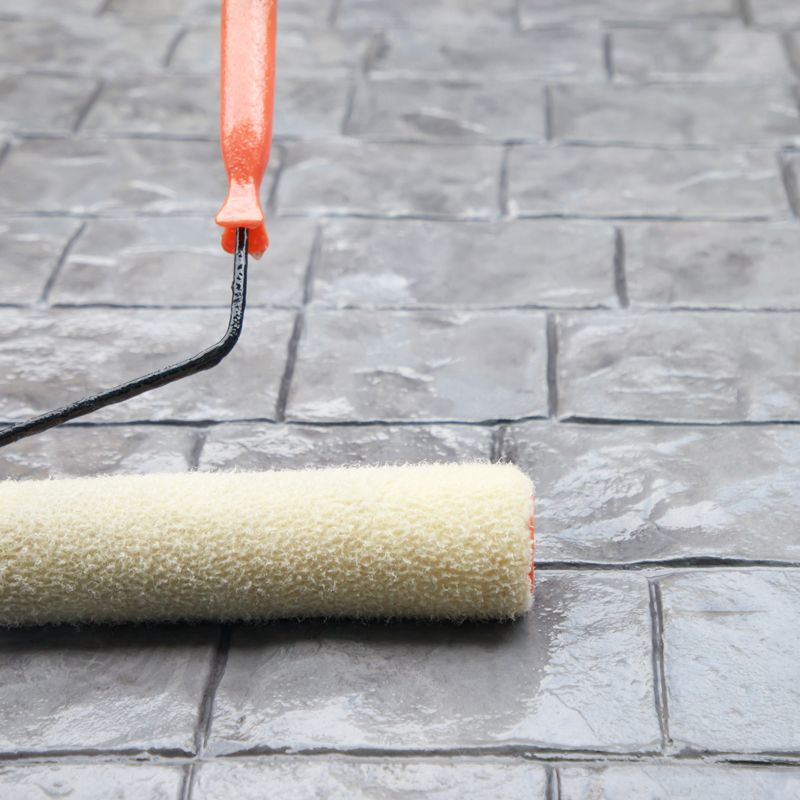 Paint roller spreading gray coating on a tiled floor
