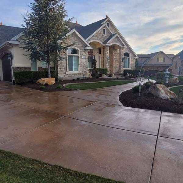 Suburban stone house with wet driveway and landscaped front yard at dusk