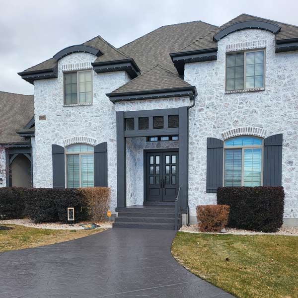 Large two-story white stone house with dark shutters and a curved driveway in front