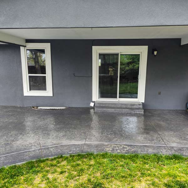 Gray house patio with concrete porch, white-trimmed windows, and sliding glass door