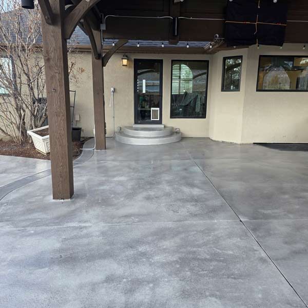 Covered entryway with concrete patio, wooden post, and glass double doors at a building entrance